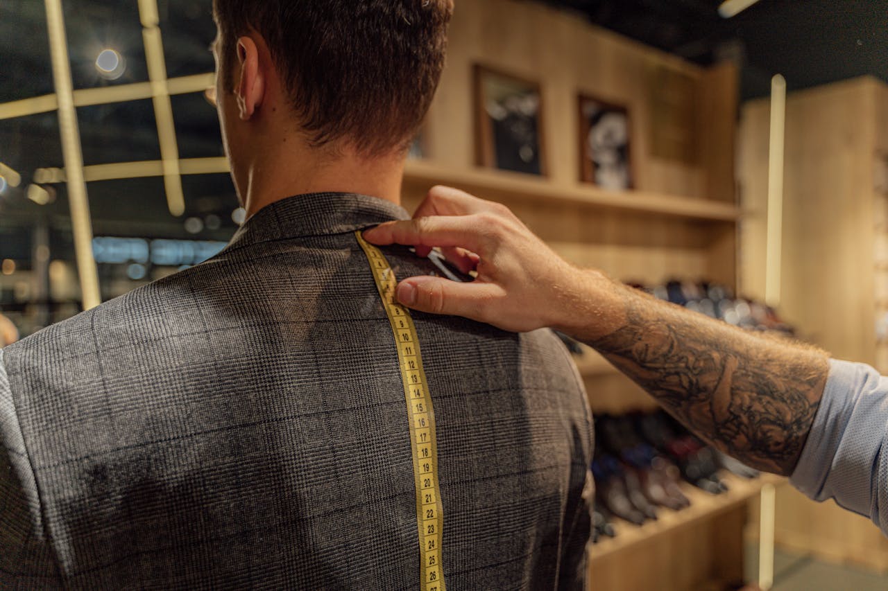 services-04 A tailor measuring a clients back with a tape inside a clothing store for a bespoke suit fitting.
